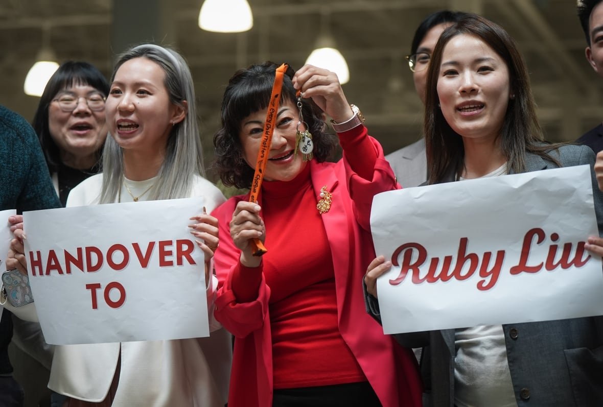 hudsons-bay-ccaa-20250626-ruby-liu-2 A group of people smile. Two of them are holding up signs reading 'handover to Ruby Liu'.