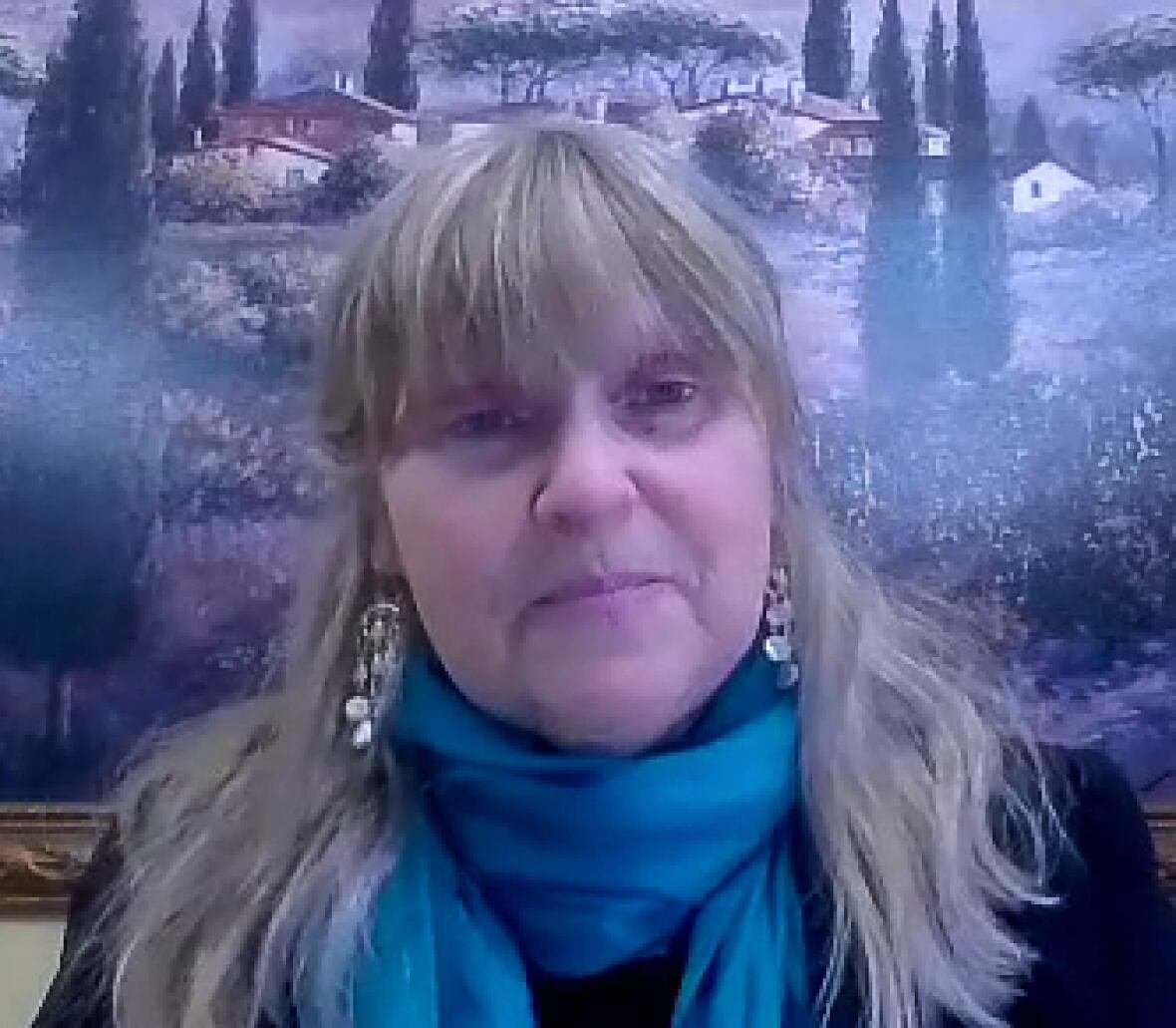 jennie-dale A woman wearing a blue scarf sits in front of a painting of a winery.