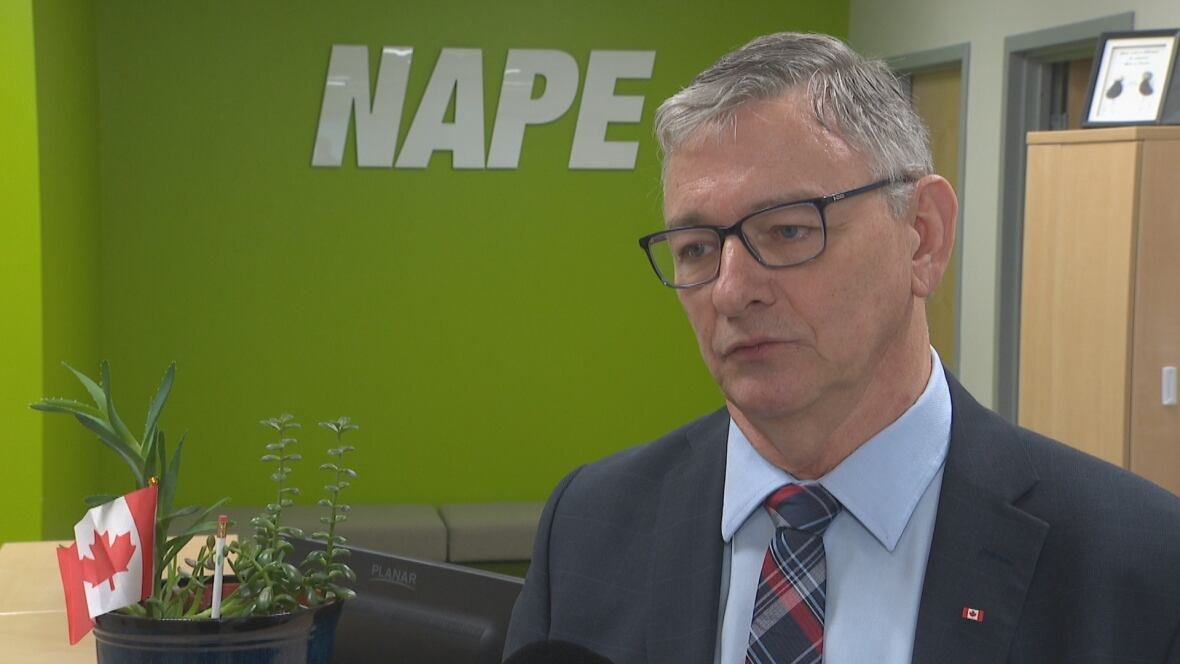 jerry-earle A man wearing a suit stands in front of a lime green wall. A sign for NAPE is hanging on the wall.