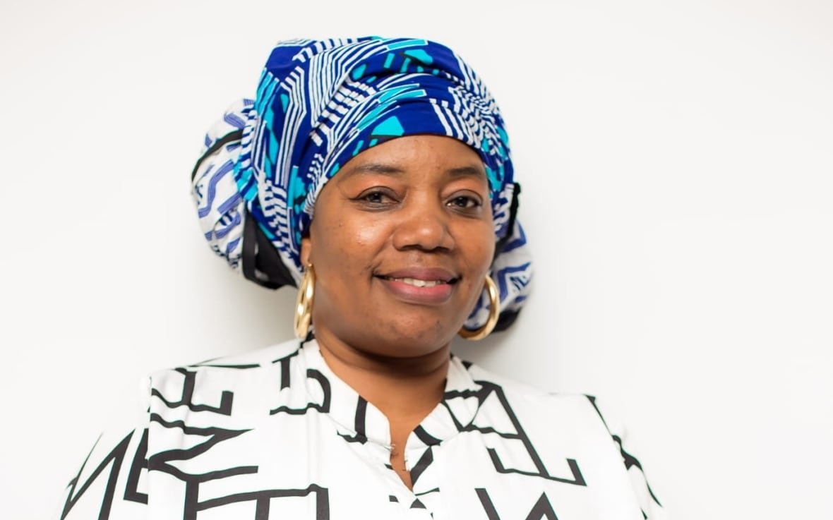 kashoro-nyenyezi A Congolese woman wearing a vibrant blue head wrap smiles at the camera for a portrait.