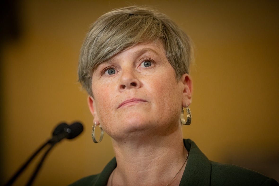 new-bc-ndp-government-cabinet-members-josie-osborne A white woman with short hair and hooped earrings is seen at a mic.