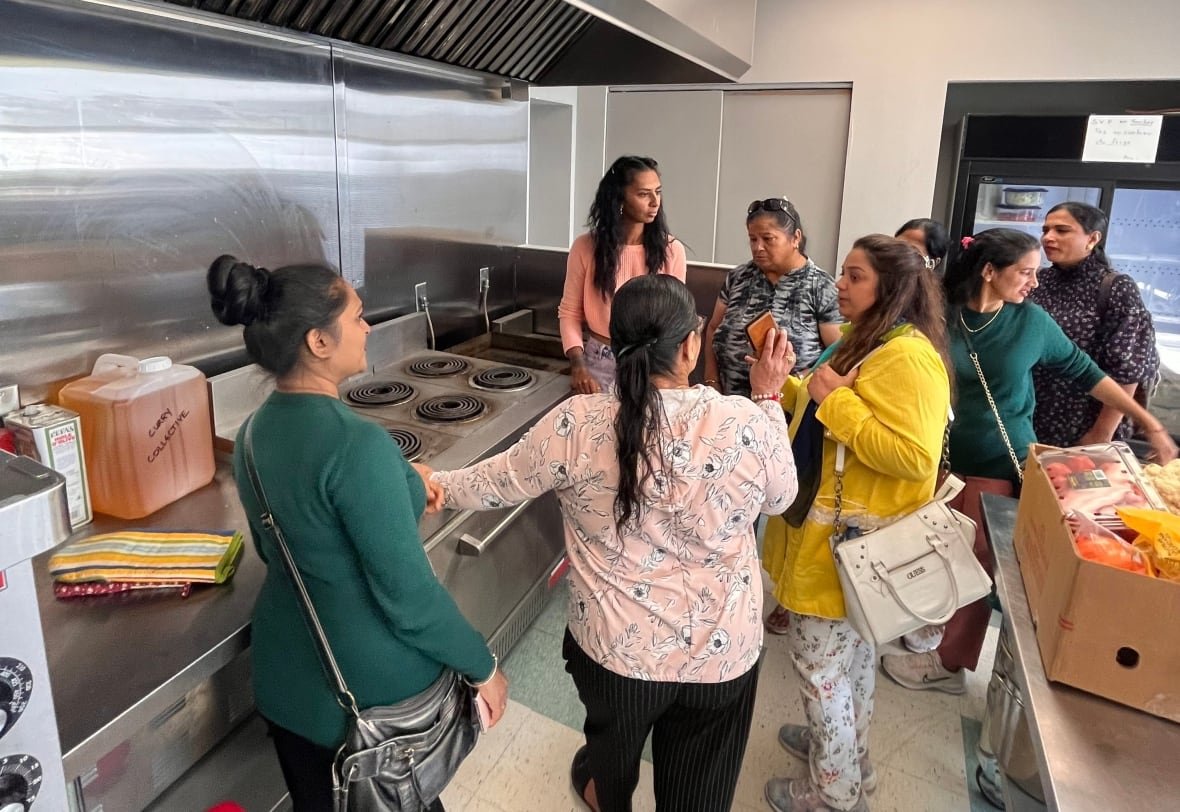 parc-ex-curry-collective A group of women discussing in an industrial kitchen.