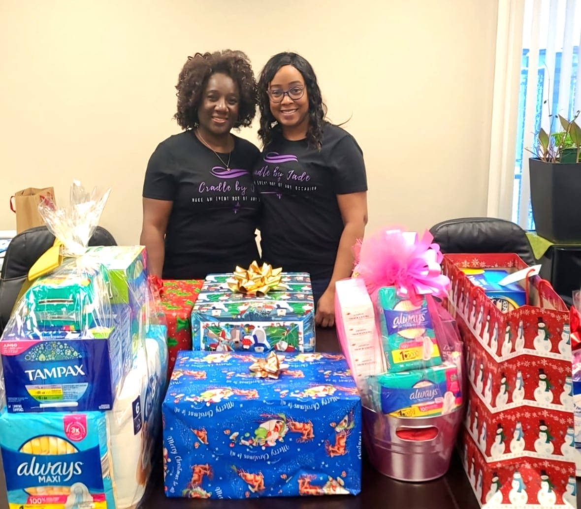petrice-dyer Two women in black shirts stand in front of a bunch of gifts.