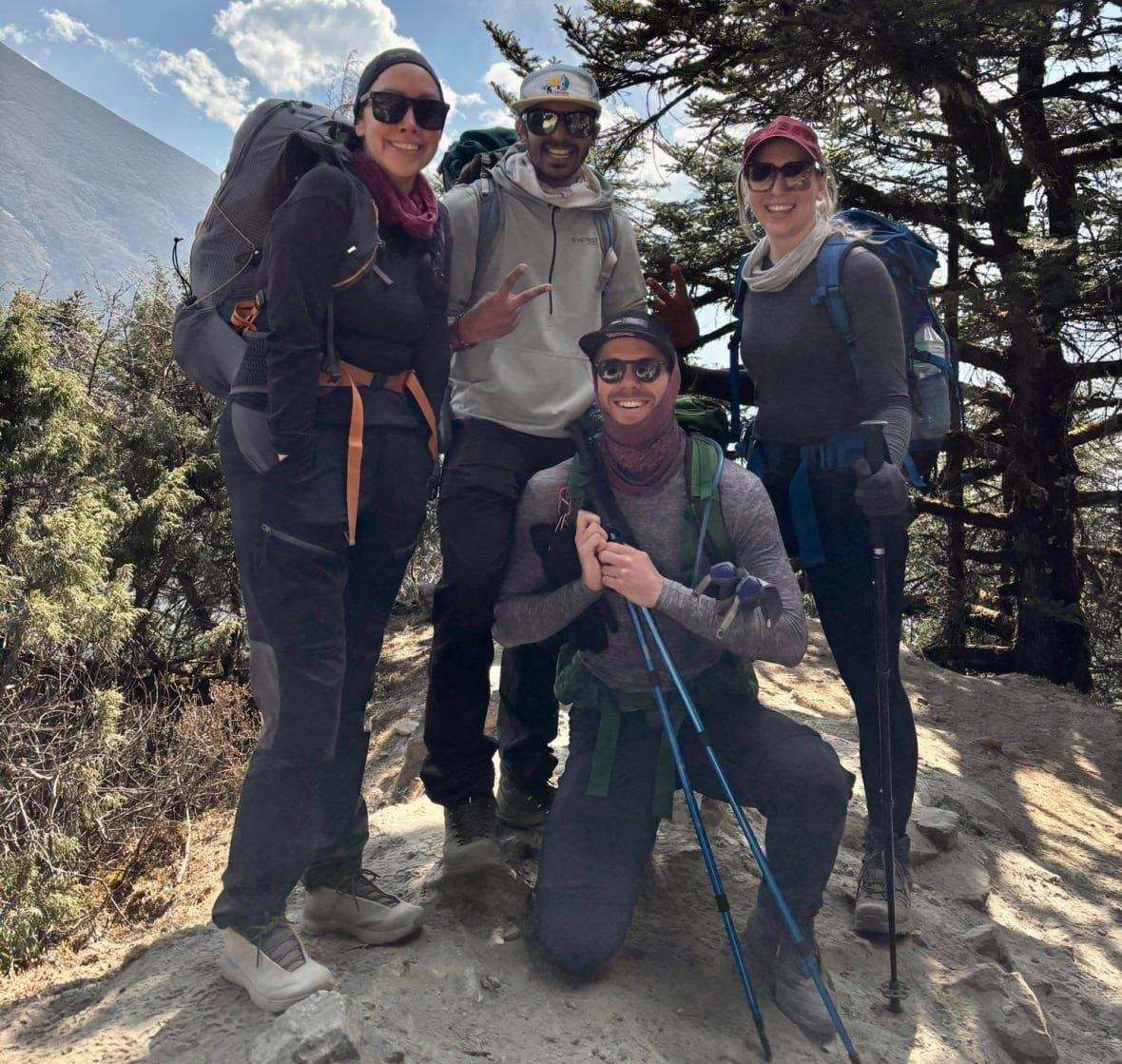 randi-gardypie-and-trekker A women wearing shades and hiking gear poses with three other people who are wearing the same type of clothing, all posing alongside a mountain.