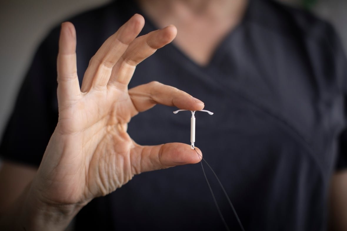 renee-hall A doctor holds up a tiny T-shaped metal object, an intrauterine device (IUD)