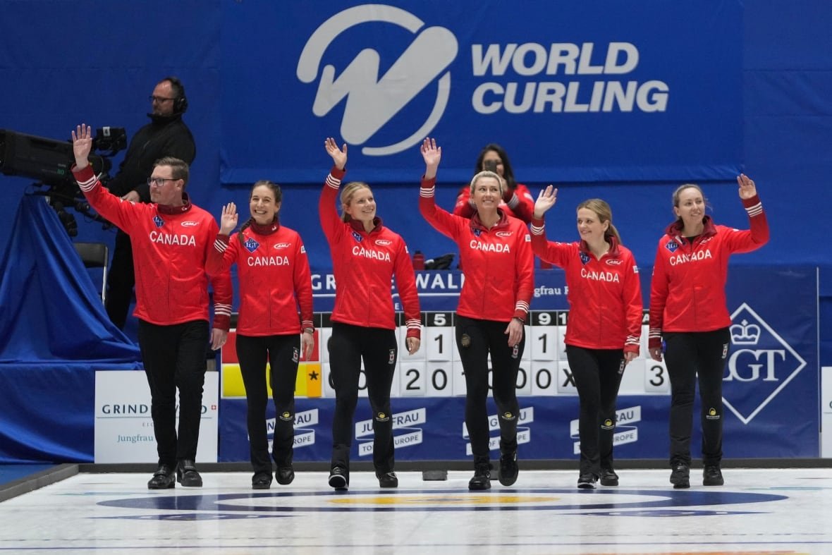 south-korea-curling-world-championship-1 A male curling coach walks alongside five women's curlers representing Canada as they all smile and wave.