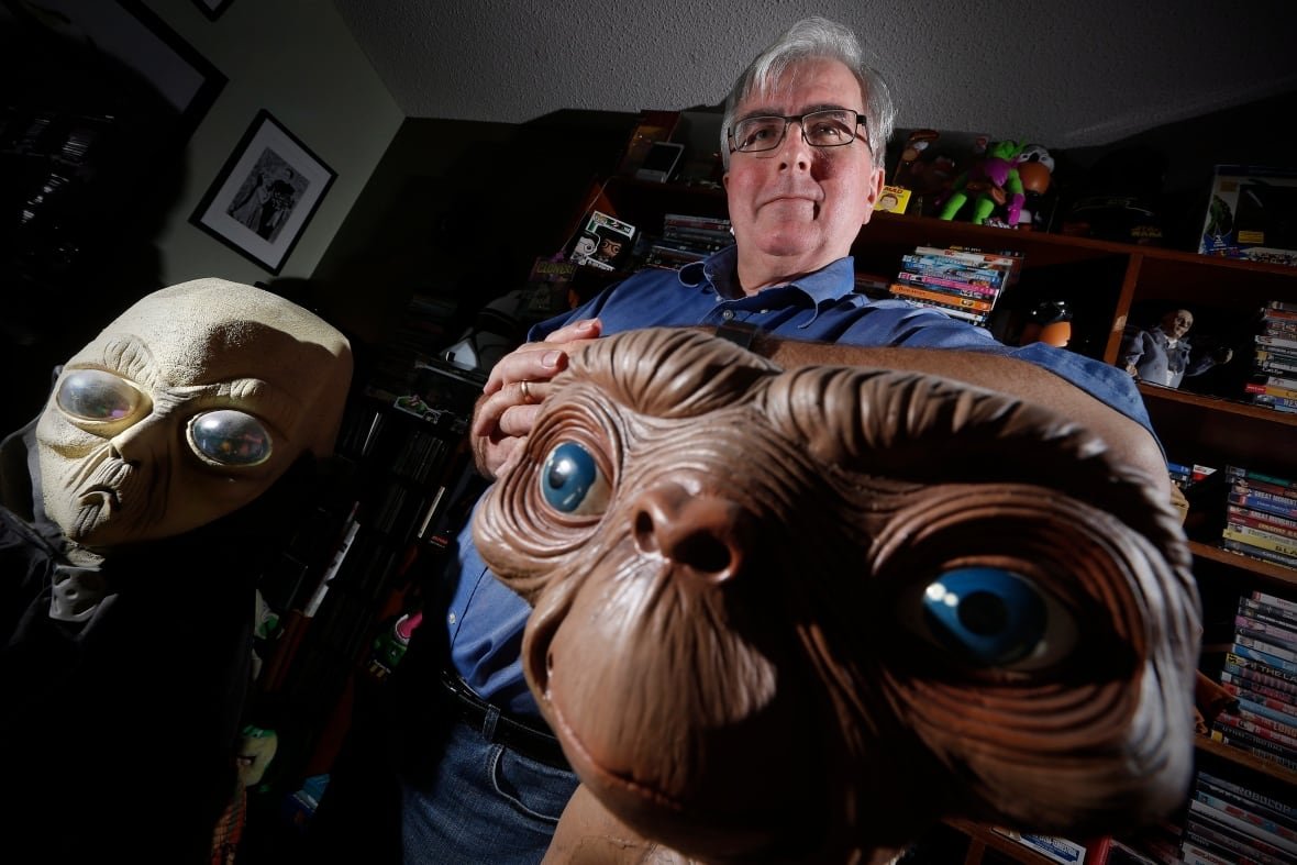 chris-rutkowski A man stands in front of two figurines of aliens.