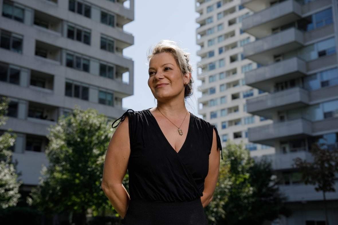 heather-hadden A woman stands on the street, two residential buildings behind her.