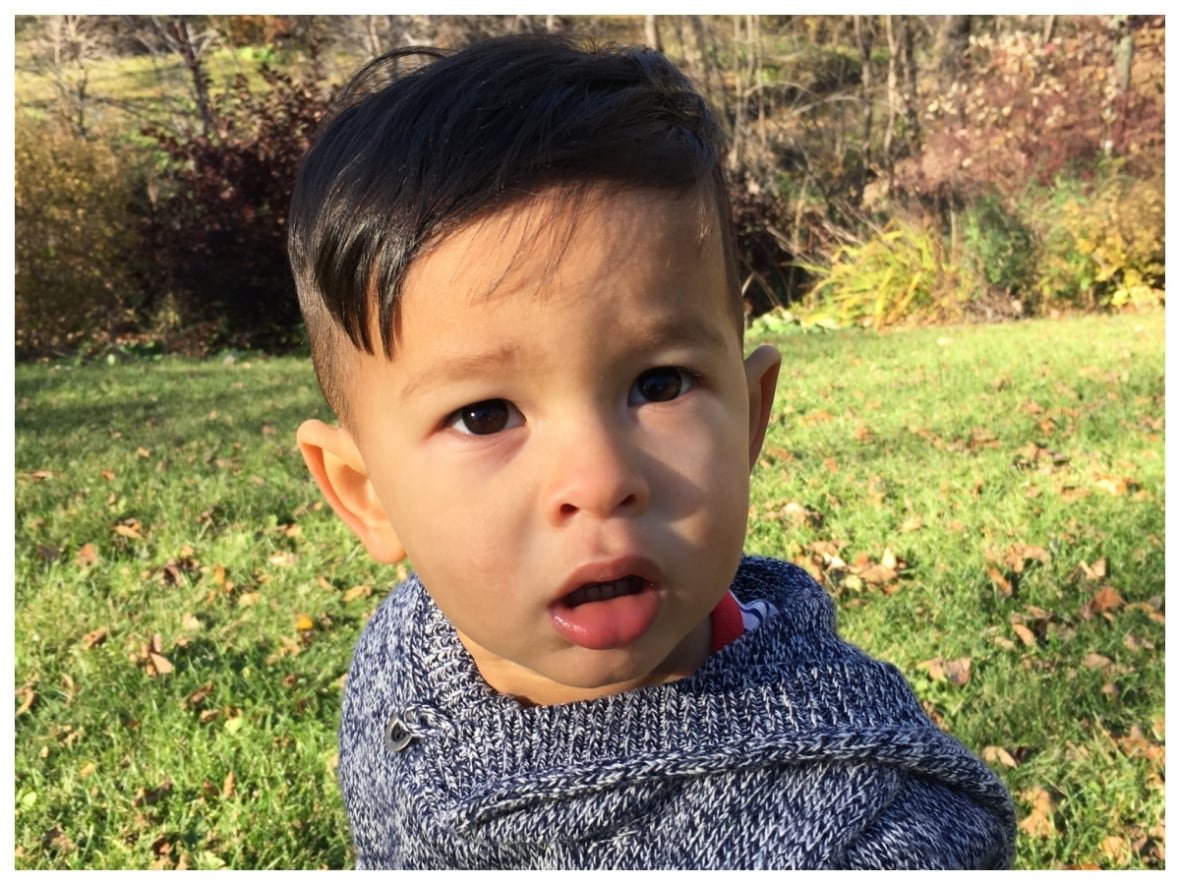 little-simon-khaoniam A curious boy sits on grass, looking towards the camera.