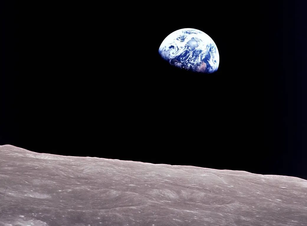 Earth viewed from a distance against a black backdrop, with the moon's surface in the foreground.