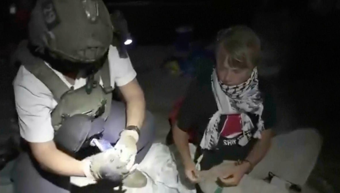mideast-wars-gaza-flotilla A person wearing a keffiyeh scarf sitting next to a soldier at night.