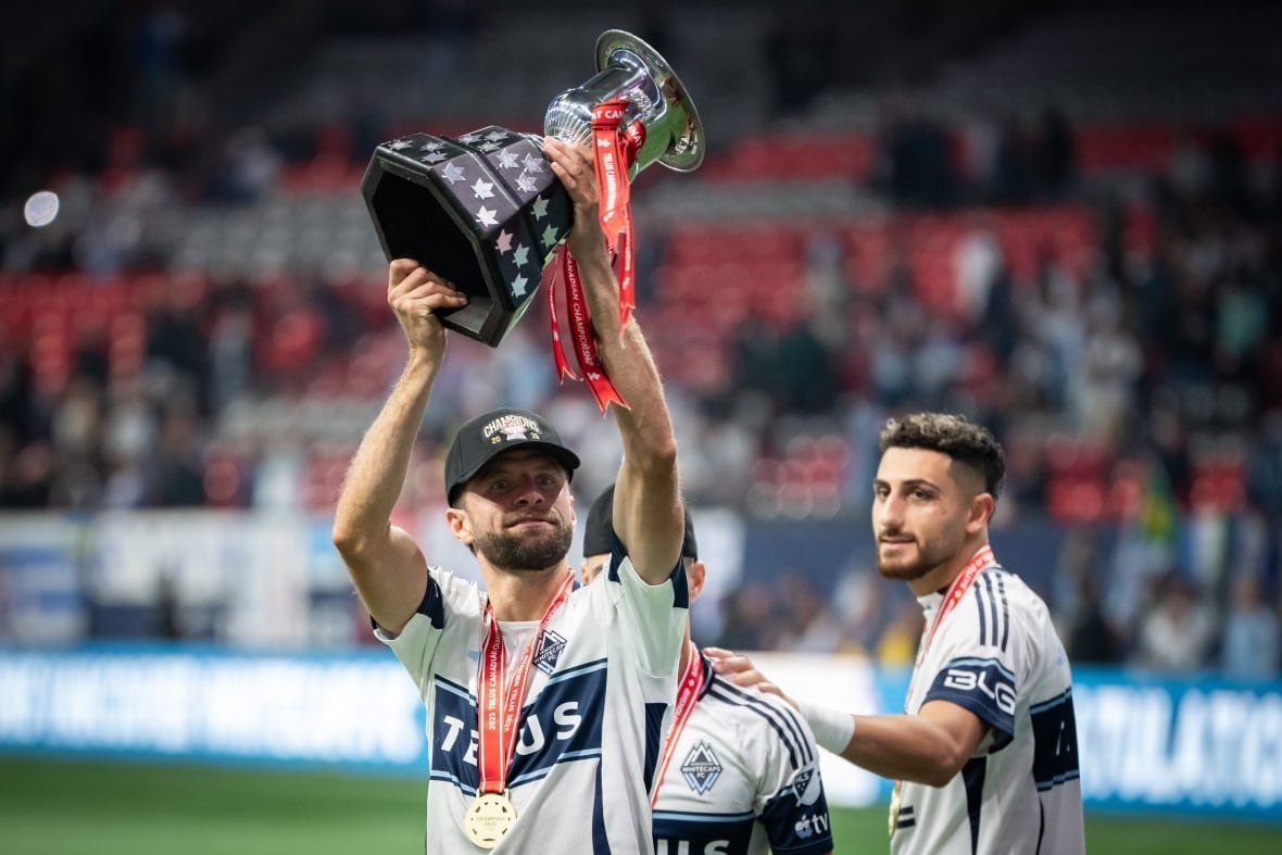 soc-vancouver-fc-whitecaps-20251001-1 Thomas Müller, sporting a black baseball hat and a medal, raises a silver cup.
