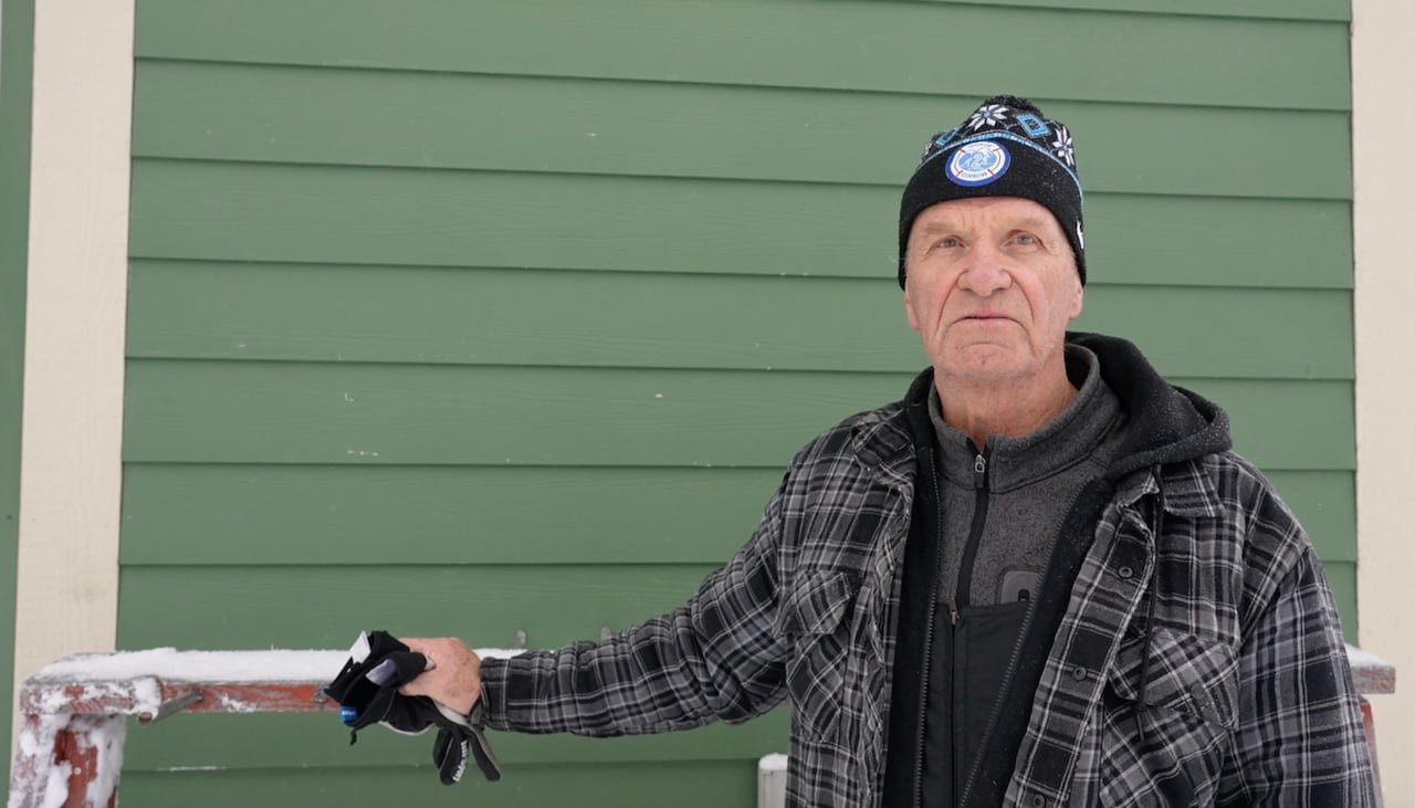 Man stands in front of a green wall and ski rack.