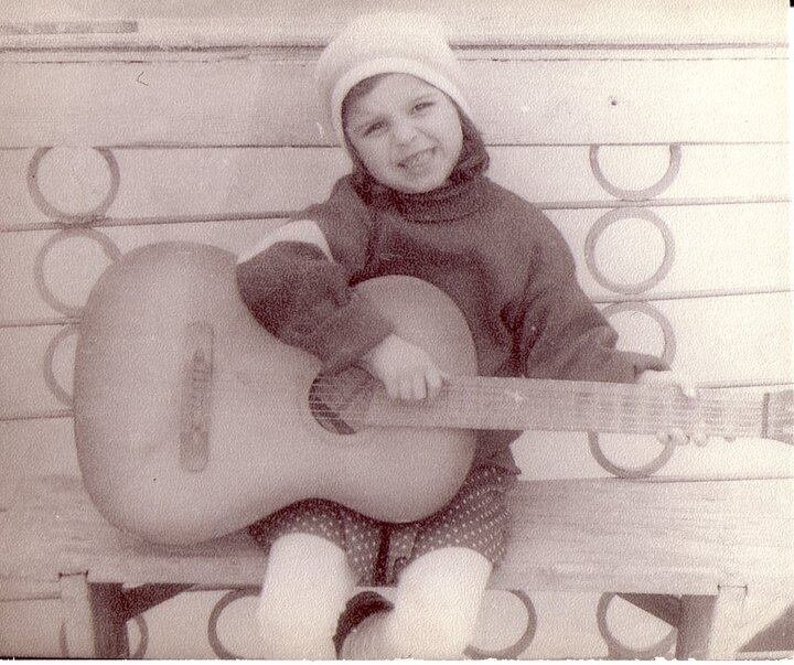 A black and white photo depicts a child holding a guitar.