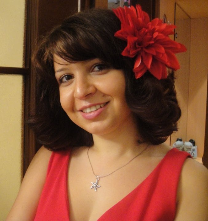A woman in a red dress with a flower in her hair smiles at the camera.