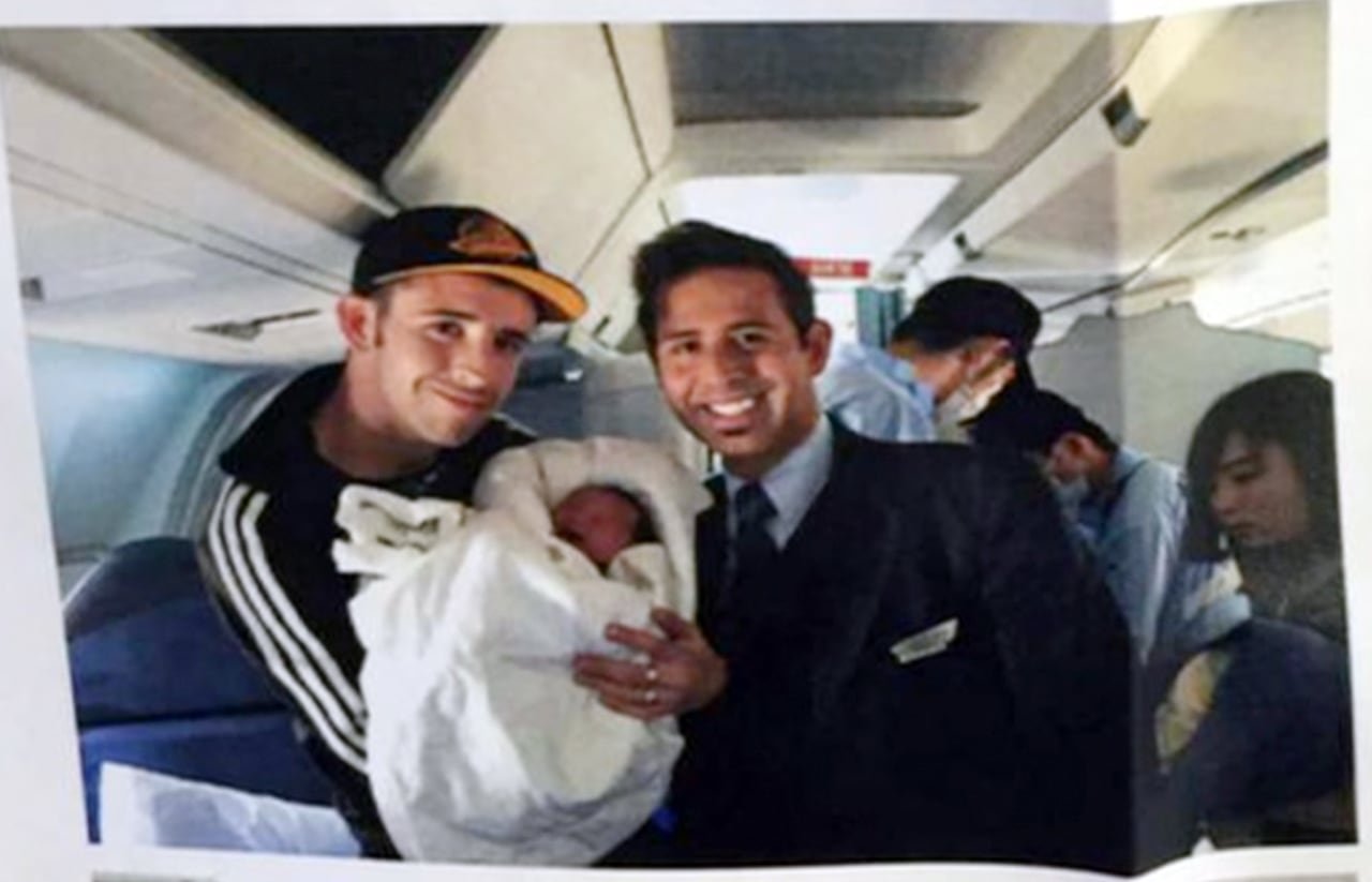 default-112 A man holding a baby on a plane, standing next to a man in uniform.