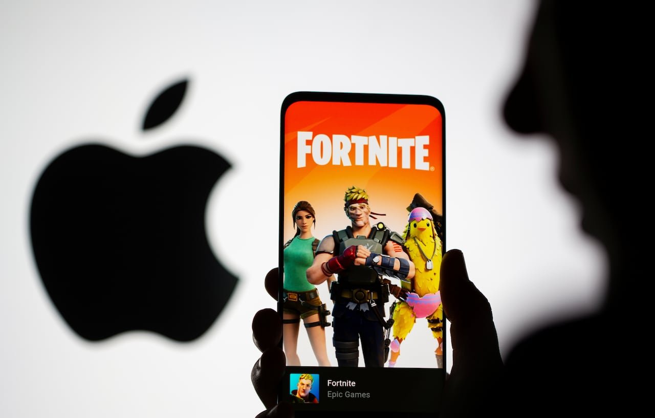 A smartphone screen showing the Fortnite logo and three game characters, with the Apple logo silhouetted in the background.