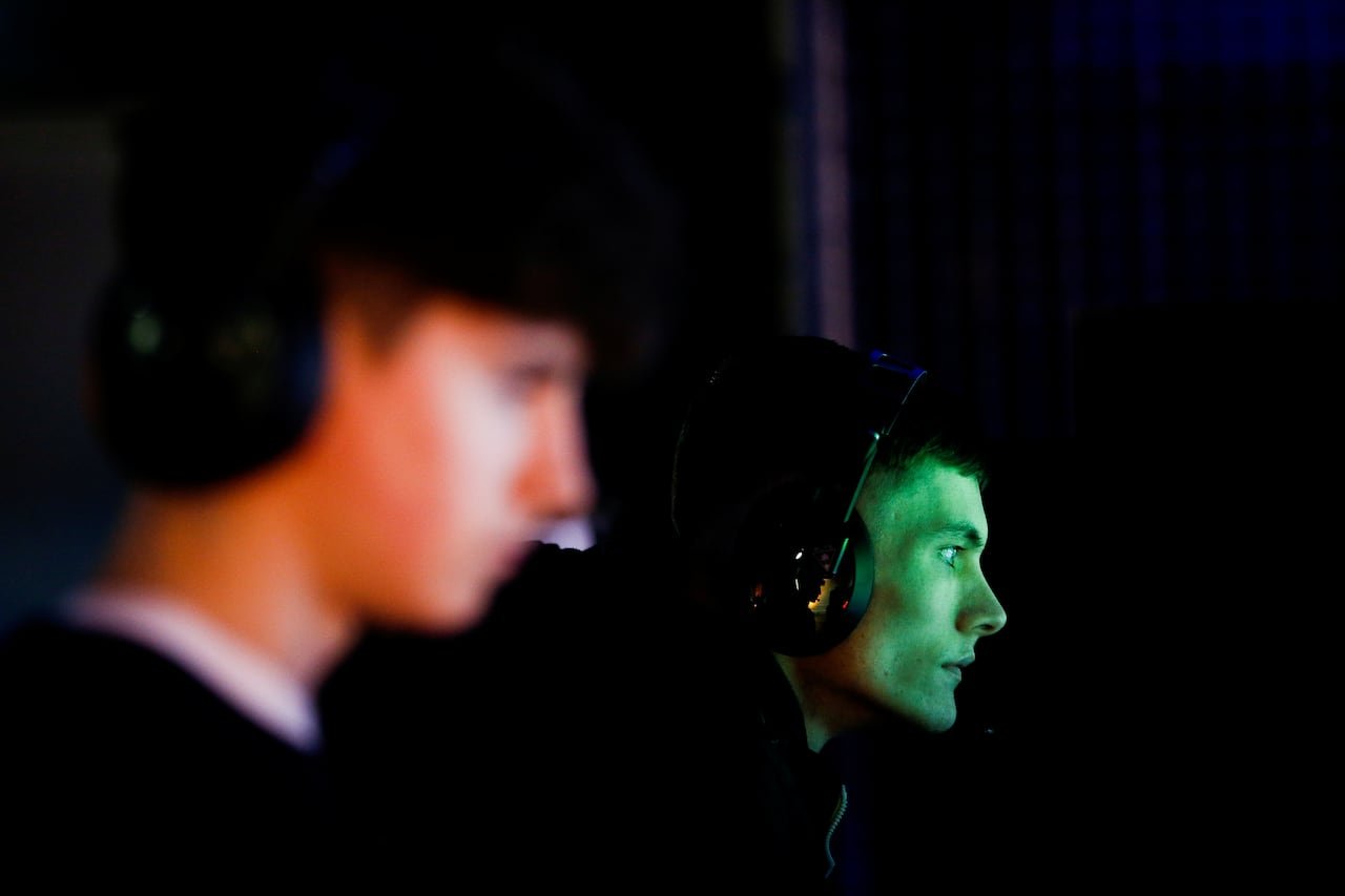 Two young men are shown in profile, one out of focus and one in focus, with the light from a screen reflecting on their faces.