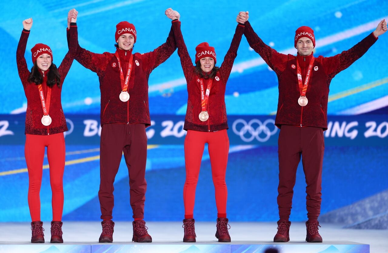 Four individuals holding hands with bronze medals hanging around their necks.