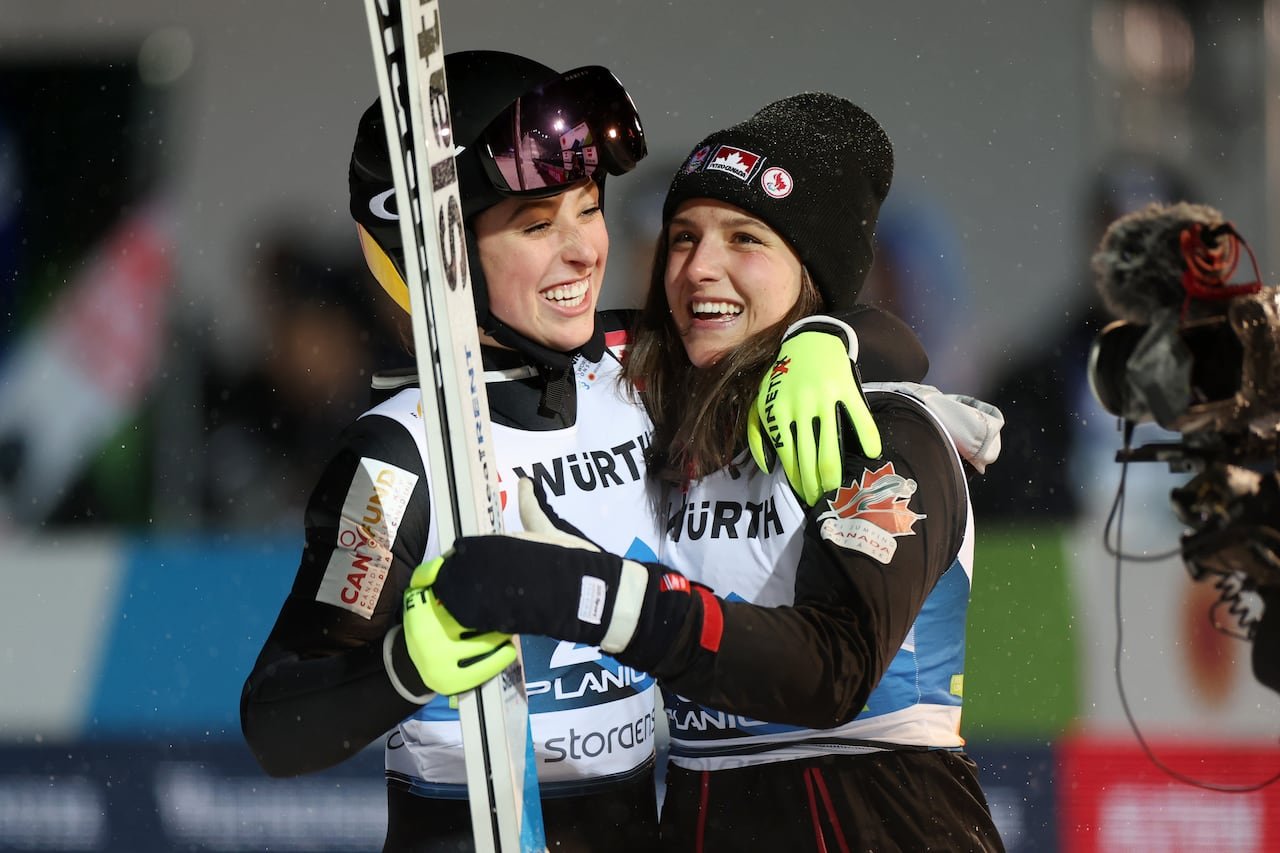 Two female ski jumpers embracing in celebration.