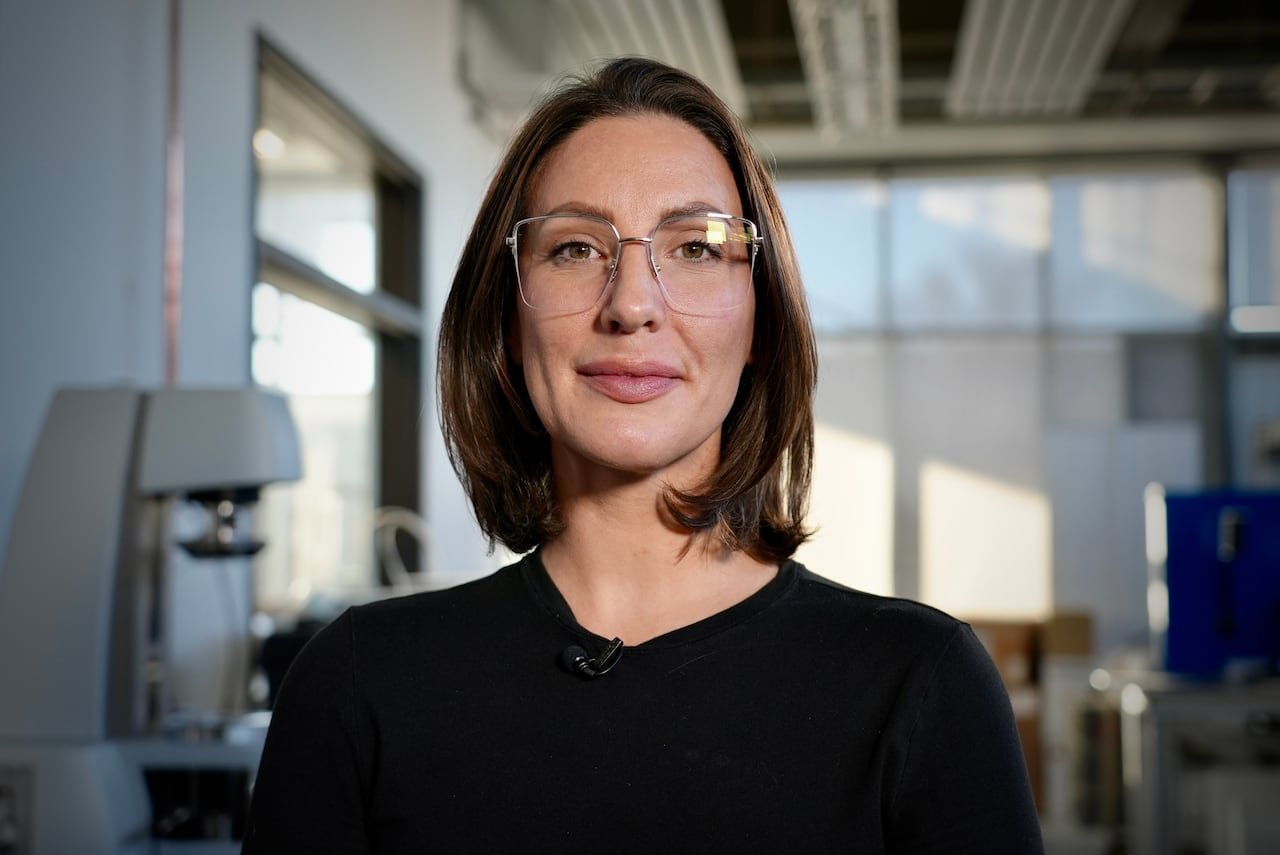 A woman with glasses and brown short hair smiles at the camera.
