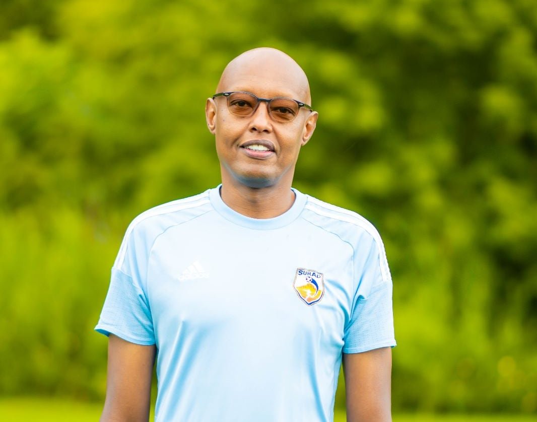A bald black man wearing a blue shirt smiles at the camera.
