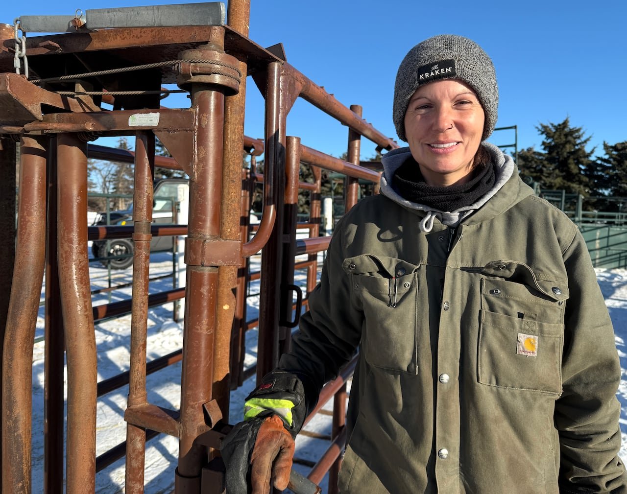 A woman in winter working clothes leans against a cattle chute.