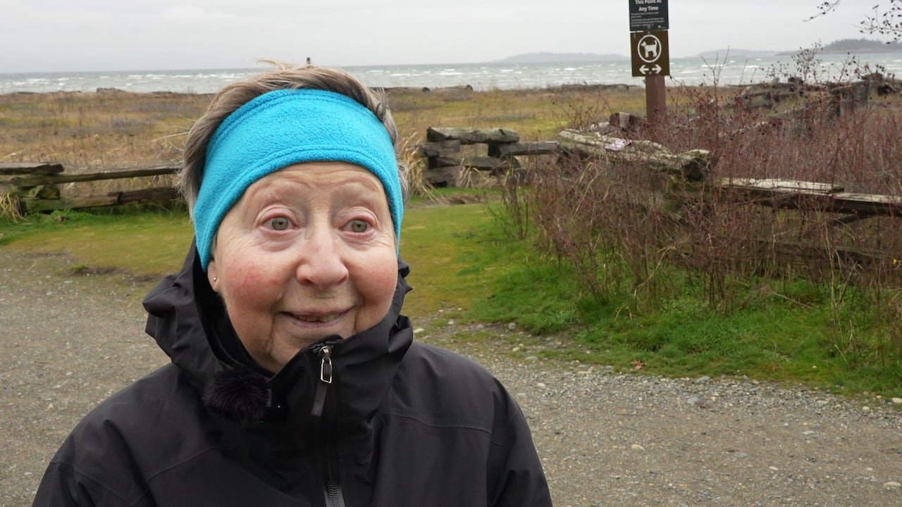 A woman with a blue headband smiles in a park.