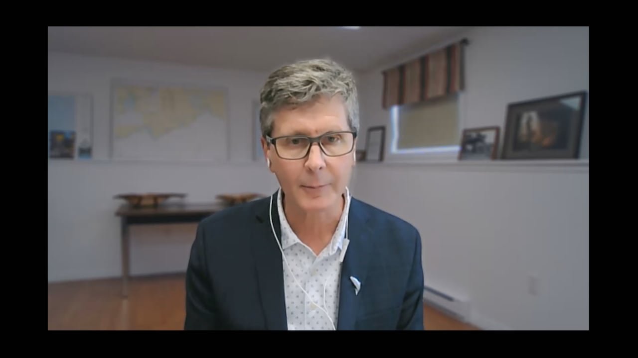 A man in a blue suit talks during a Zoom interview.