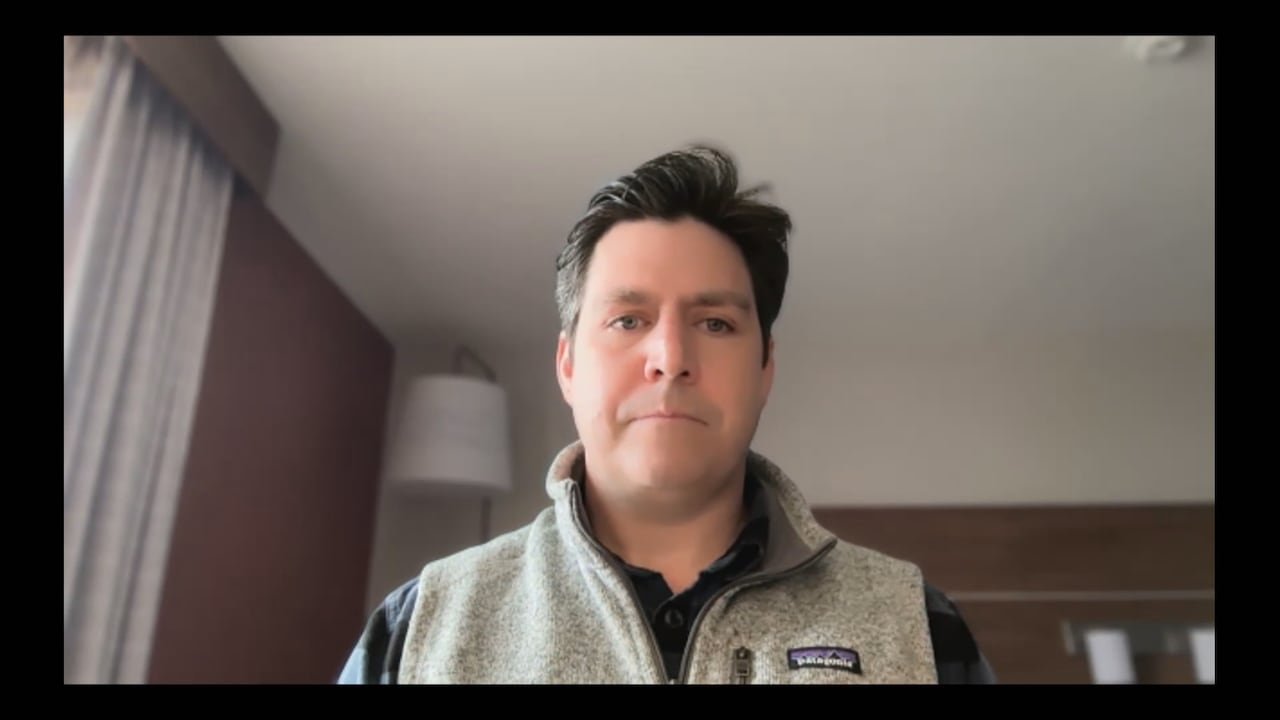 A man in a Patagonia vest is seen speaking on a Zoom call.