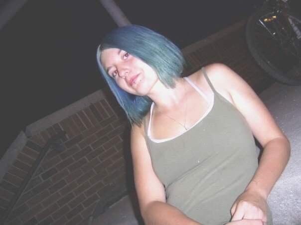 A woman with blue hair poses for the camera with a small smile