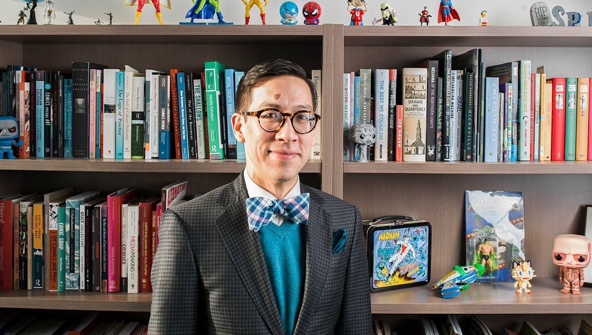 default-431 Man in suit and bow tie standing in front of a bookshelf filled with books.