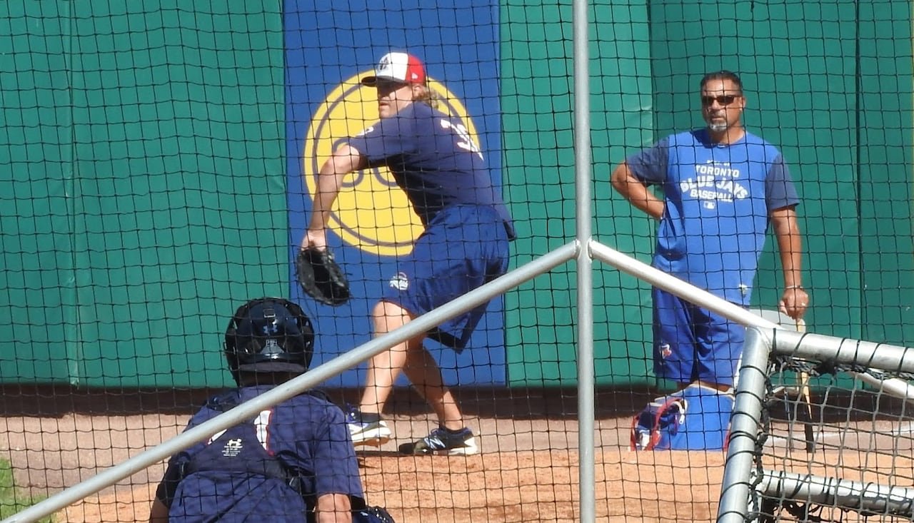 default-511 A pitching coach looks on as a player throws to a catcher.