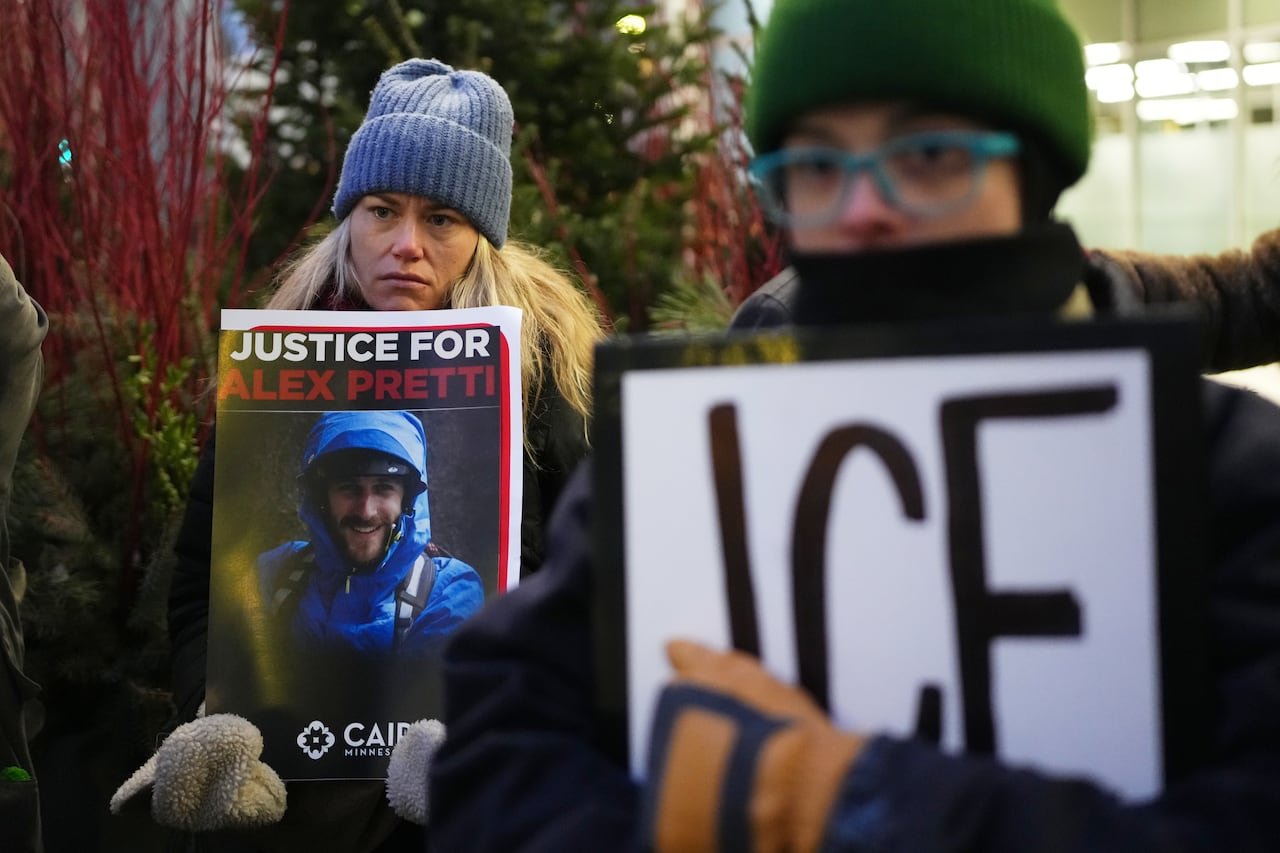 default-137 A woman with long blonde hair, wearing clothing, stands outside holding an image of a man. The sign says 'Justice for Alex Pretti."