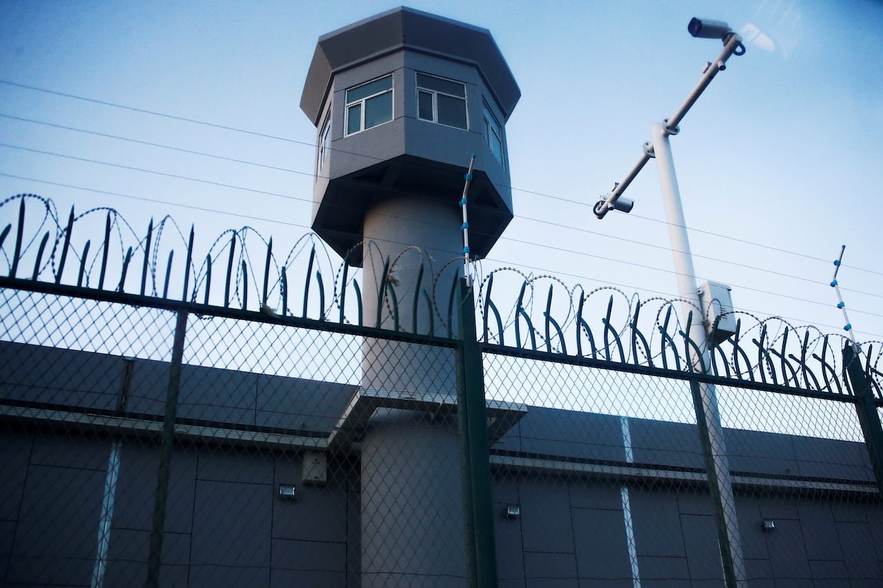 A watchtower behind a chicken-wire fence topped with barbed wire and metal spikes.