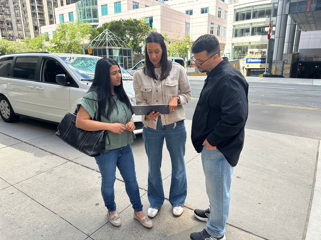 default-674 Three people stand and look at a tablet on the sidewalk with a van parked behind them.