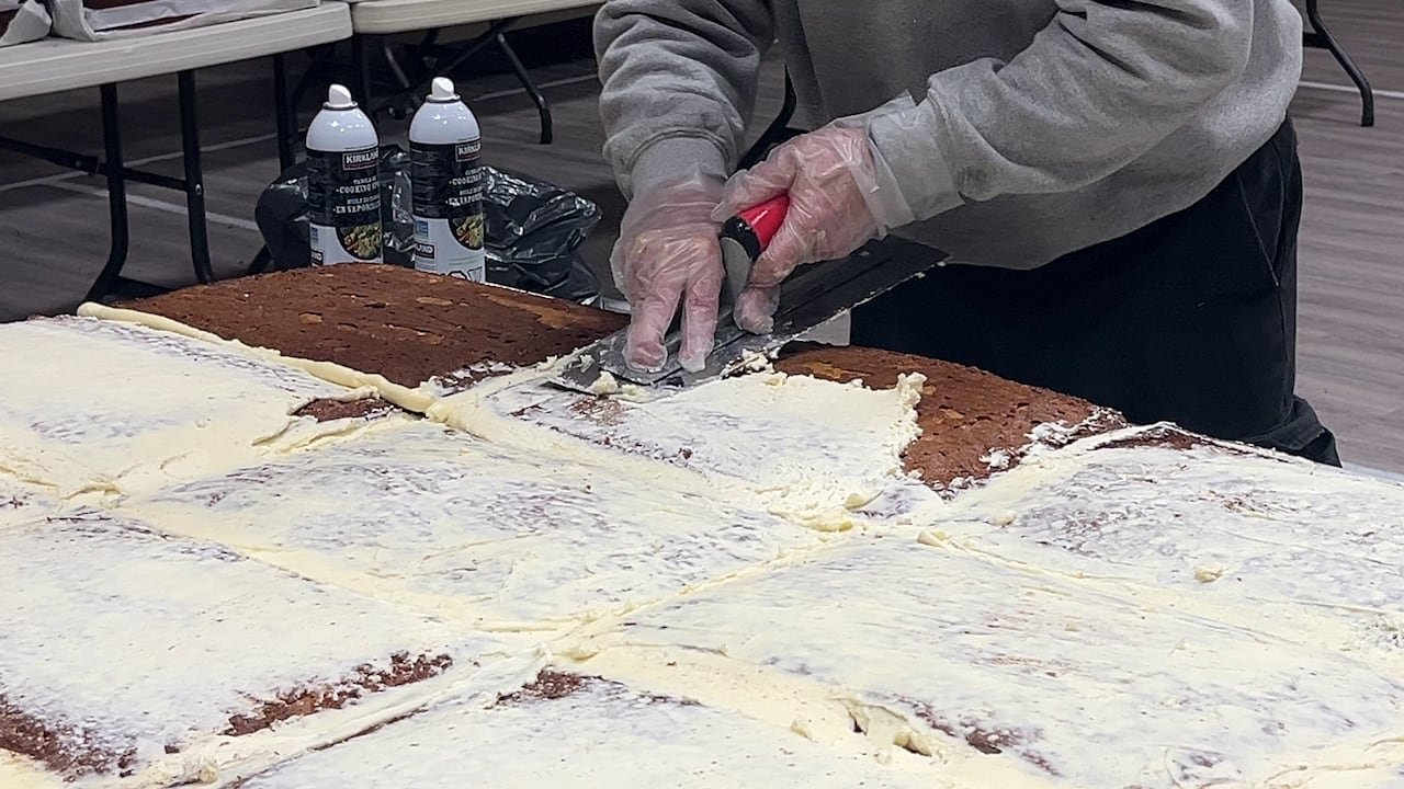 default-343 A person using a scraper to apply icing to a huge series of cakes.