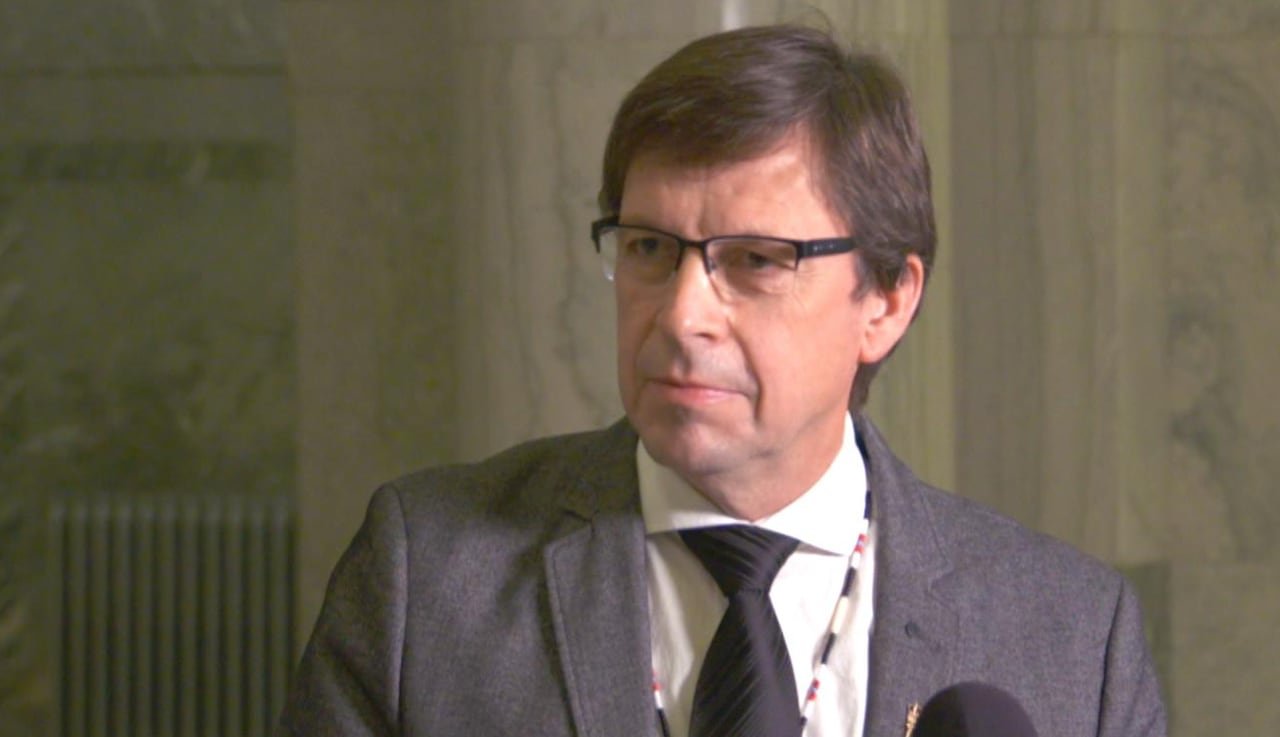 A man with glasses stands and looks at a reporter.