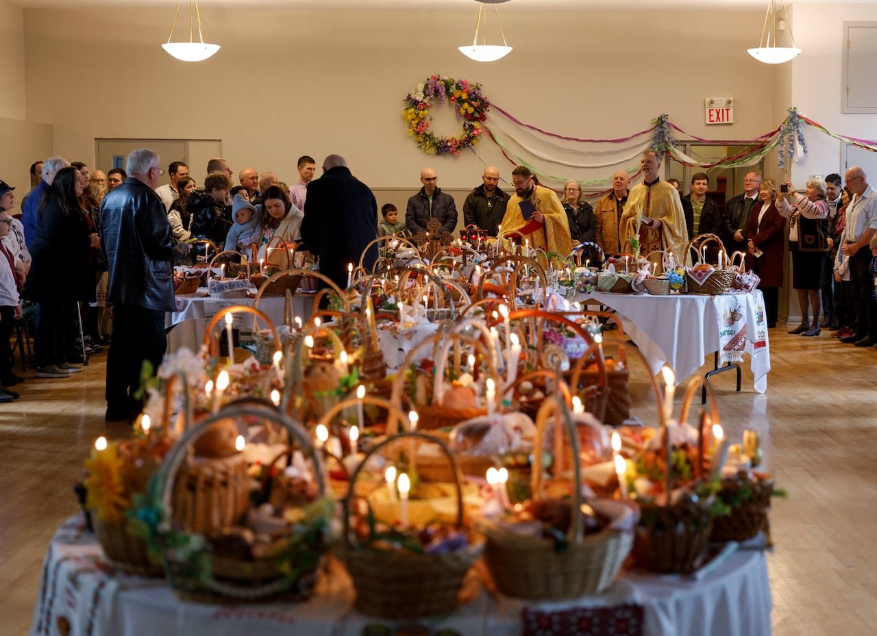 default-230 Food baskets with lit candles on white-clothed tables, with people at the back of a church room.