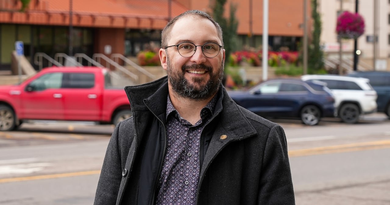 A politician smiling in front of a brick building in Fort McMurray.