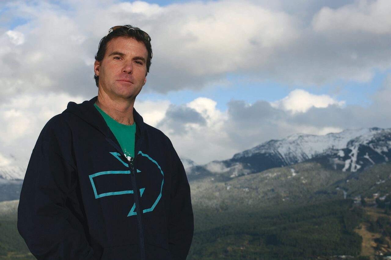 A man looks at the camera with a mountain pictured behind him.